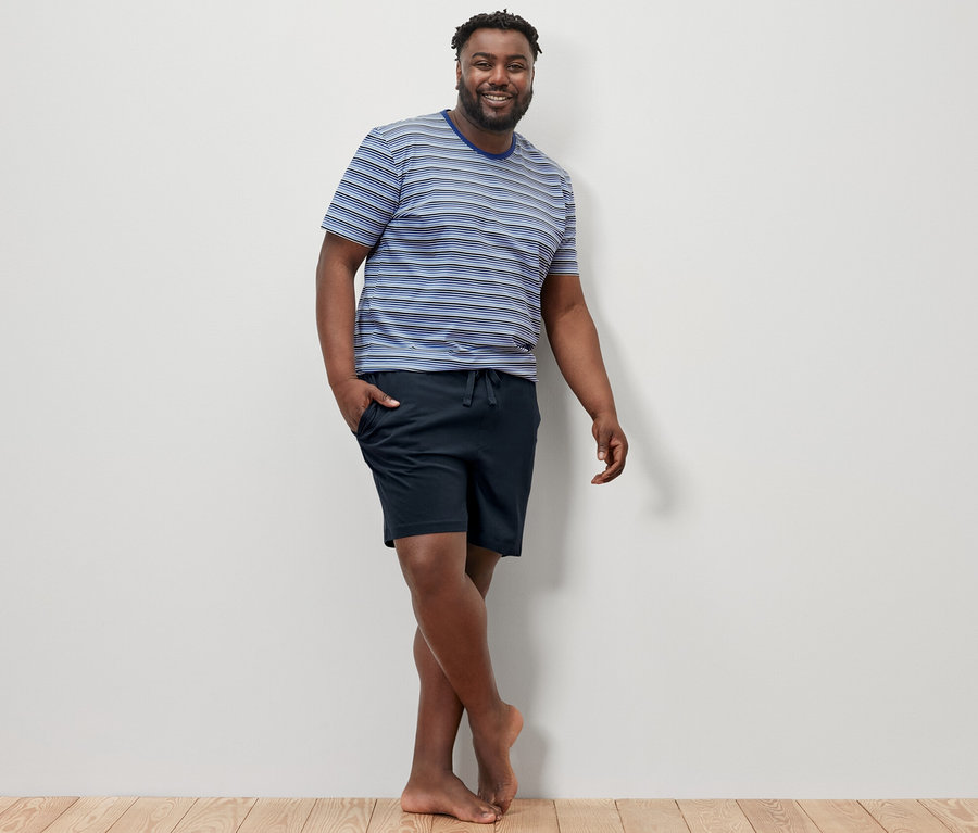 Un homme pose sur un plancher en bois et porte un pyjashort bleu et bleu foncé.