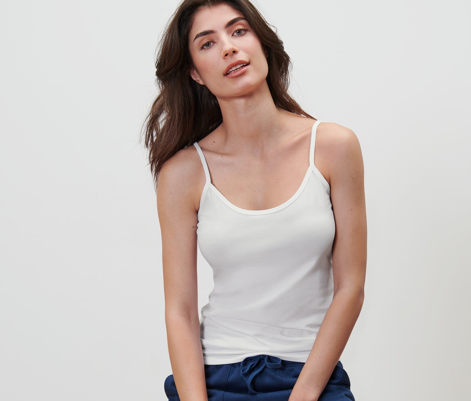 Une femme est assise sur un tabouret et porte une chemisette blanche à bretelles spaghetti d'un ensemble de 5.