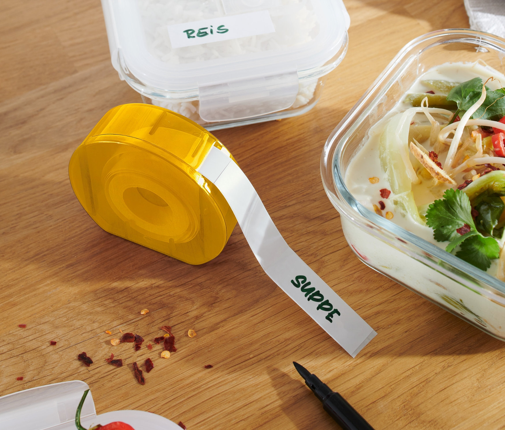 Distributeur d'étiquettes jaune sur une table en bois à côté de récipients contenant du riz et de la soupe.