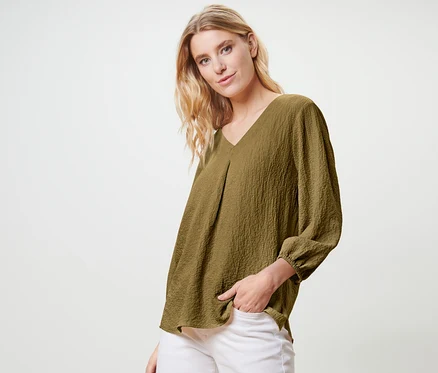 Blonde posant en chemisier-tunique vert olive et pantalon blanc.