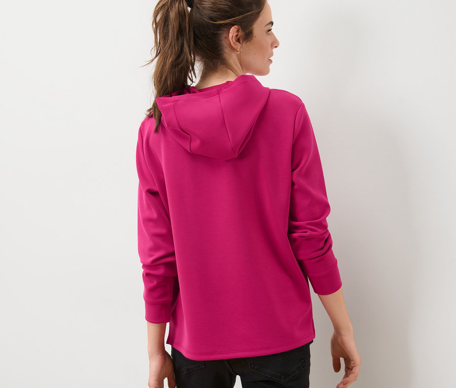Une femme vue de dos porte un pull à capuche rose en mélange de modal.