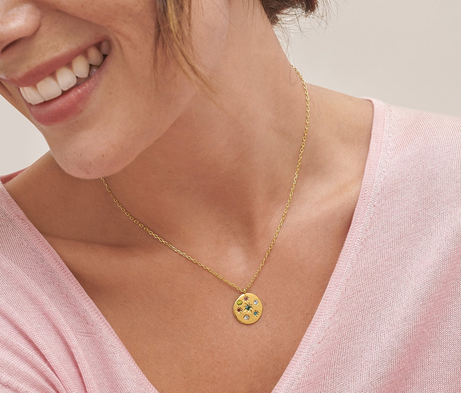 Gros plan d'une femme souriante portant une chaîne avec pendentif rond multicolore et des créoles avec pendentifs multicolores.