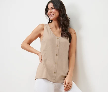 Une femme souriante pose, vêtue d'un haut beige chiné avec une patte de boutonnage et d'un pantalon blanc.