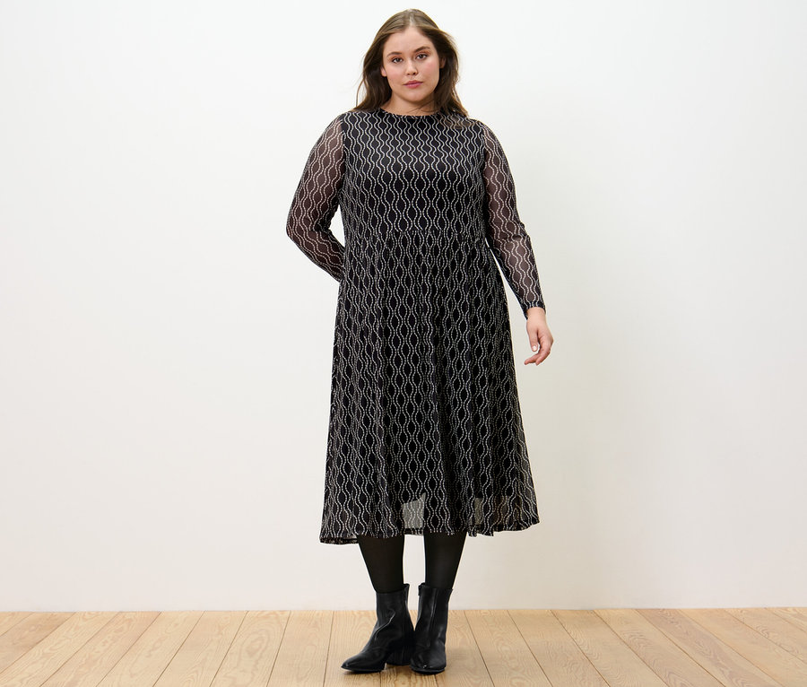 Une femme debout porte une robe en mesh imprimée.