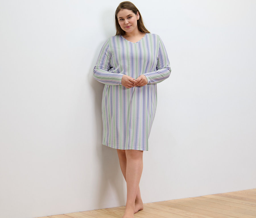 Femme en chemise de nuit rayée debout près d'un mur.