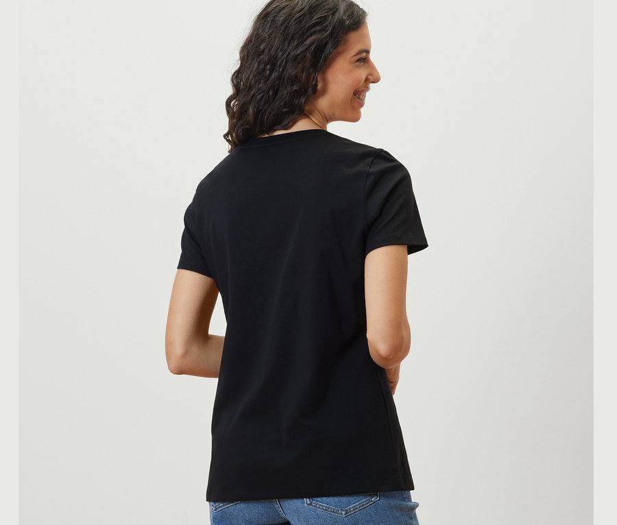 Une femme regarde par-dessus son épaule et porte un t-shirt basique noir.
