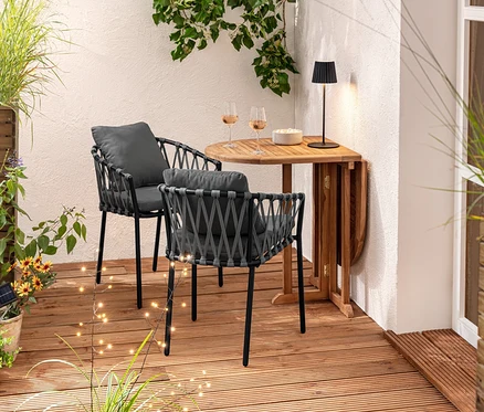 Deux fauteuils pour table à manger avec tressage textile sont placés près d'une table en bois. Des verres et un bol sont posés sur la table. À l'arrière-plan, on voit un séparateur d'espace pour jardinière et 3 piquets solaires.