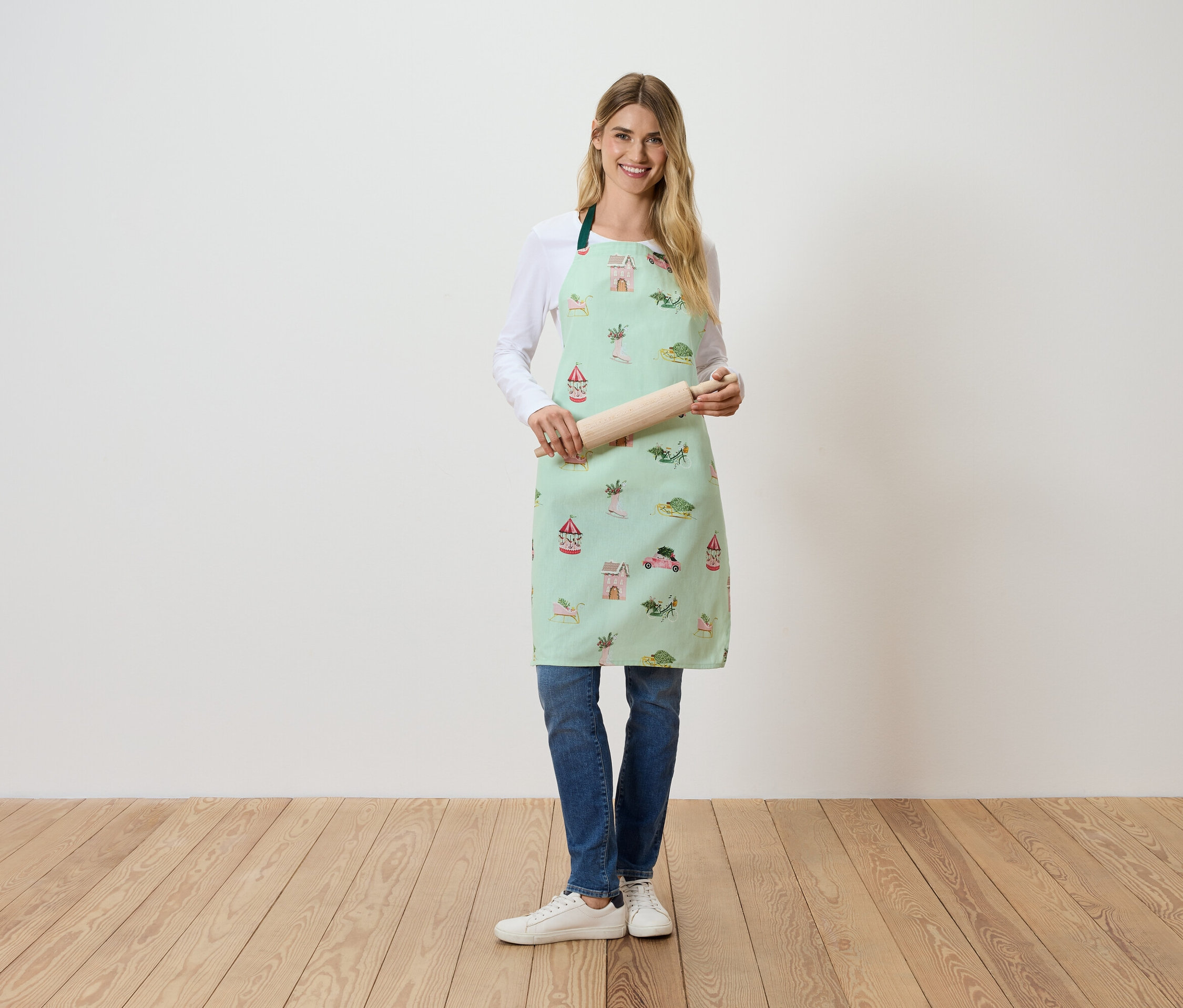 Une femme debout tient un rouleau à pâtisserie. Elle porte un tablier vert clair avec un imprimé.