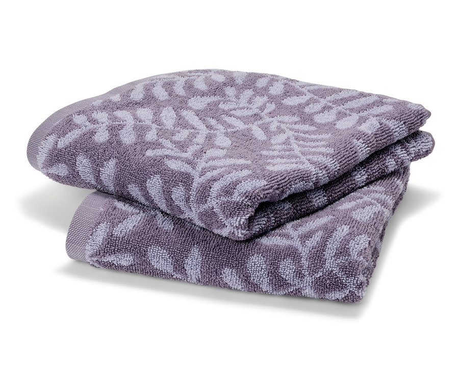 Deux serviettes de bain en tissu éponge lilas pliées l'une sur l'autre. Les serviettes ont un motif de feuilles délicat.