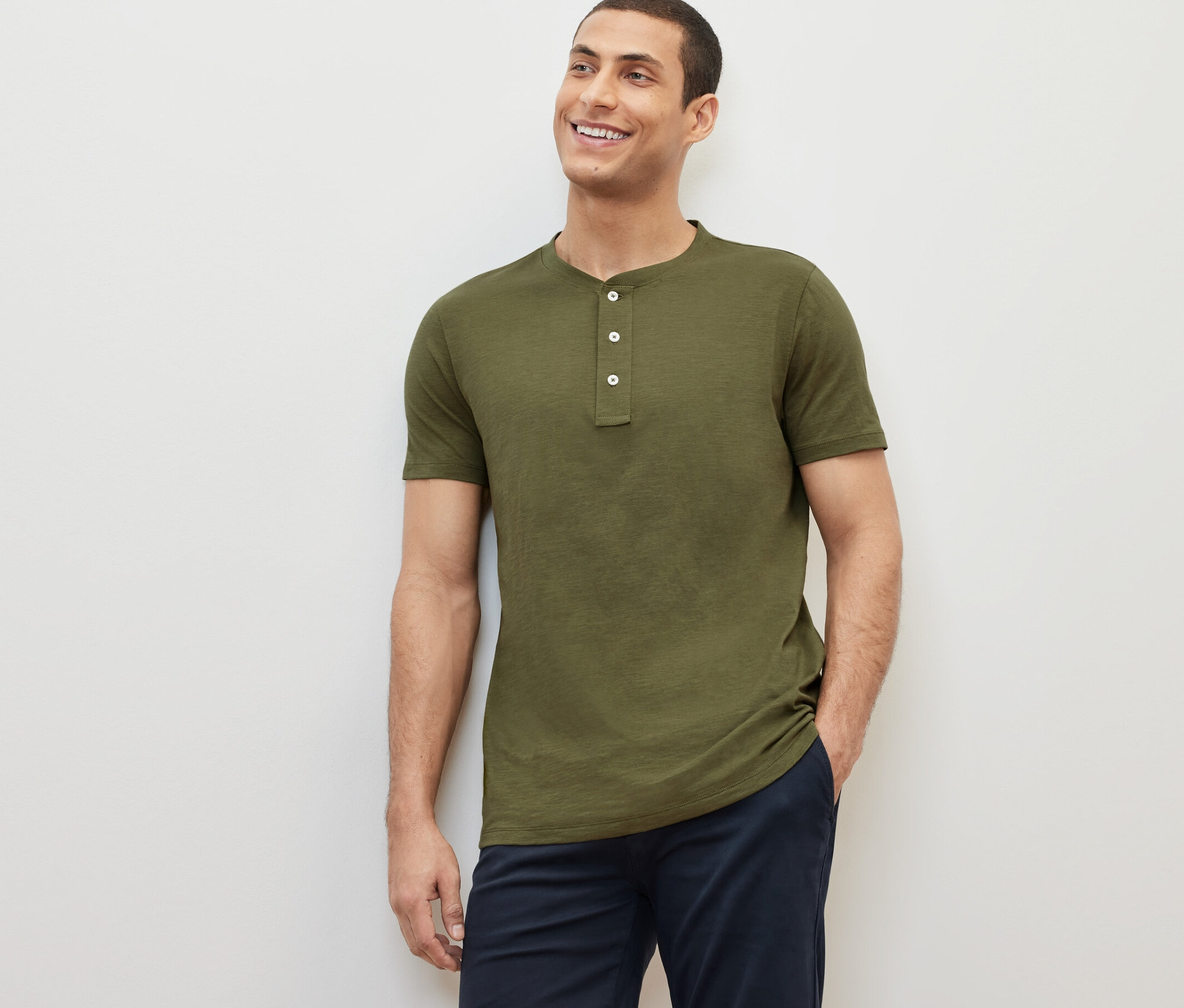 Un homme souriant pose, portant un Henley kaki à manches courtes.