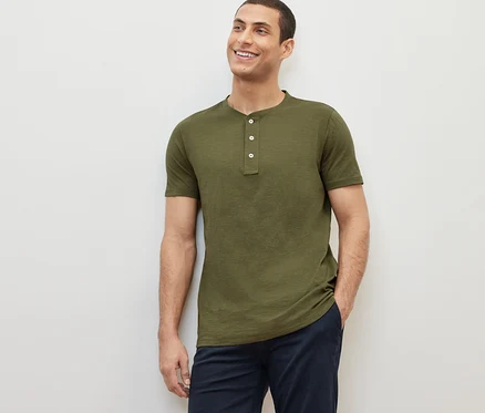 Un homme souriant pose, portant un Henley kaki à manches courtes.