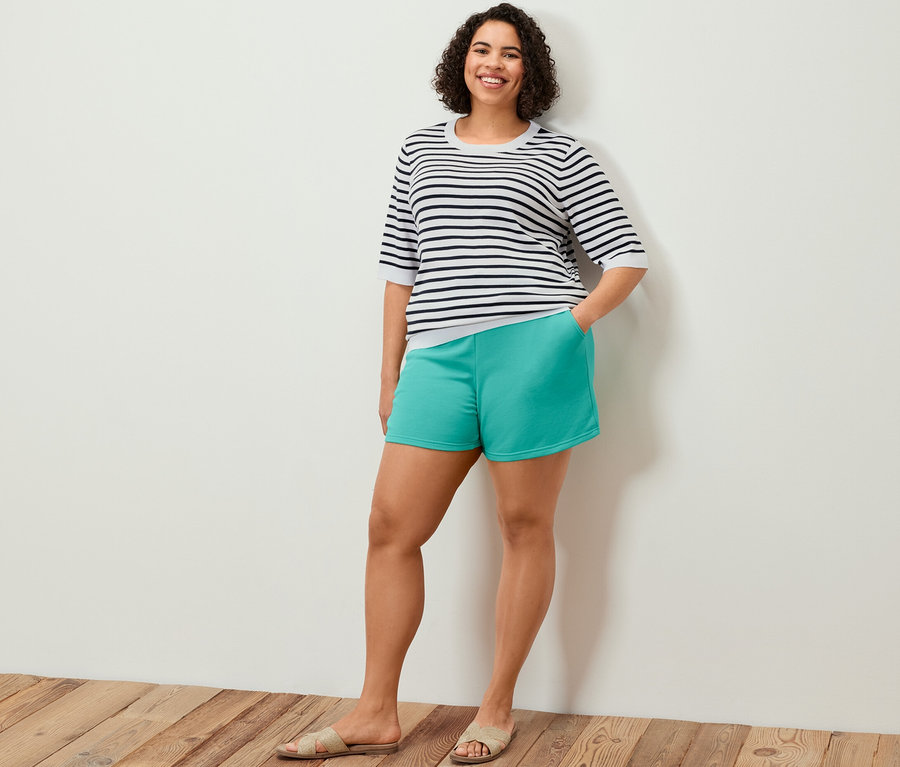 Femme posant en short molletonné turquoise et pull en tricot fin à rayures bleu marine.