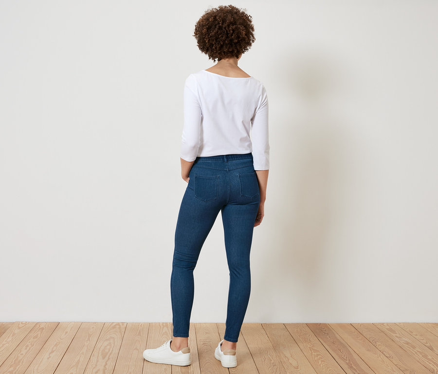 Vue arrière d'une femme aux cheveux bouclés portant une chemise blanche et un jean bleu.