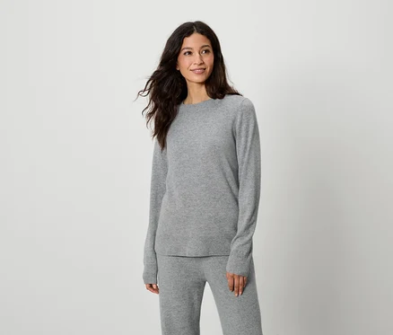 Femme posant en pull et pantalon gris.