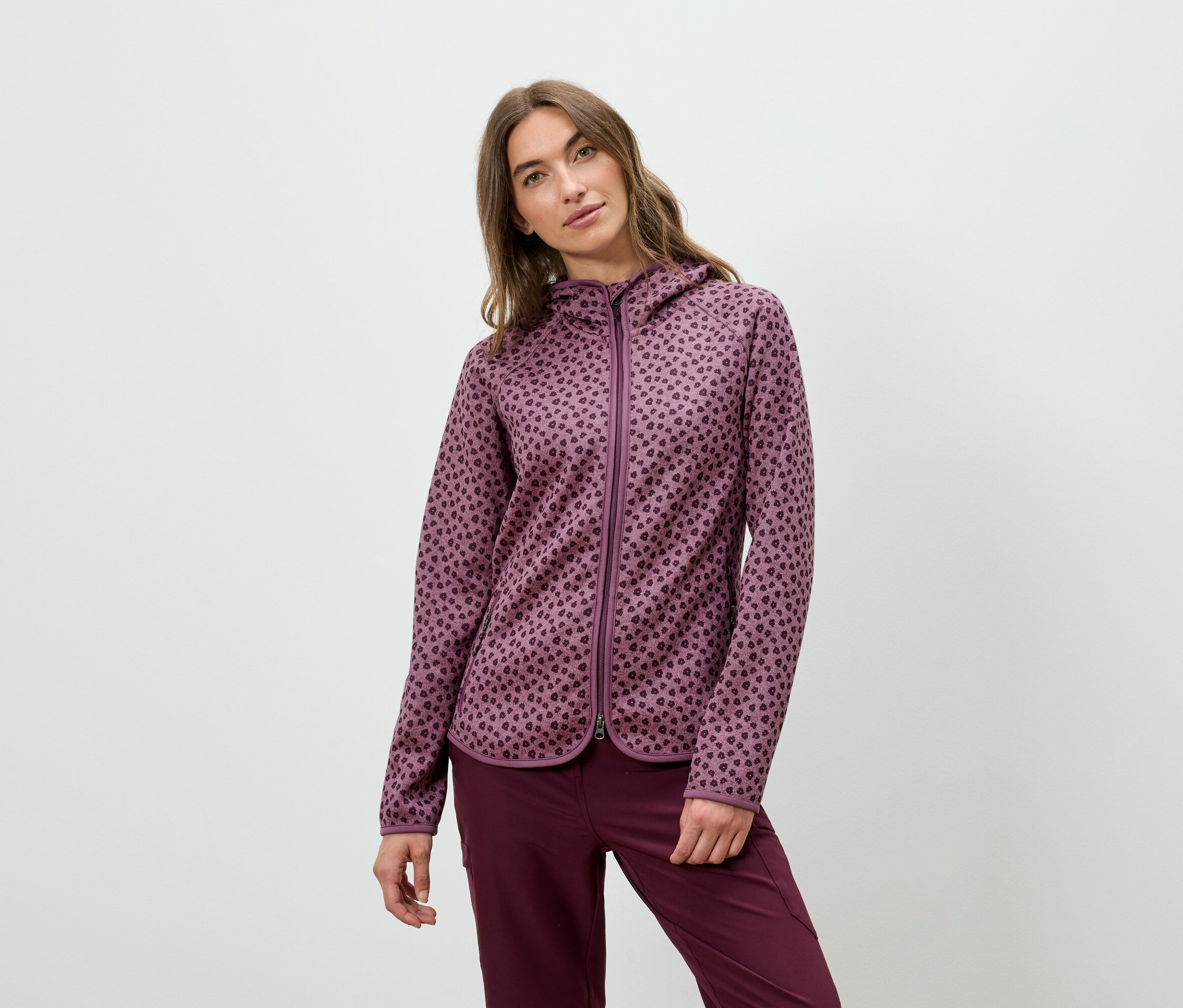 Une femme pose dans un sweat à capuche bordeaux et un pantalon.