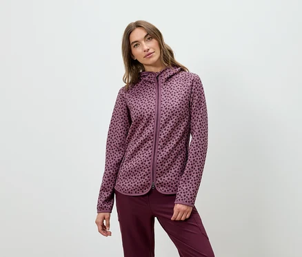 Une femme pose dans un sweat à capuche bordeaux et un pantalon.