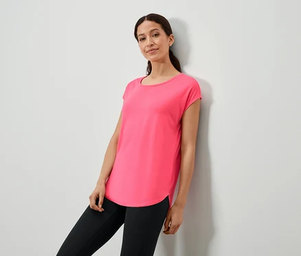 Femme appuyée contre un mur portant un t-shirt rose et un legging noir.