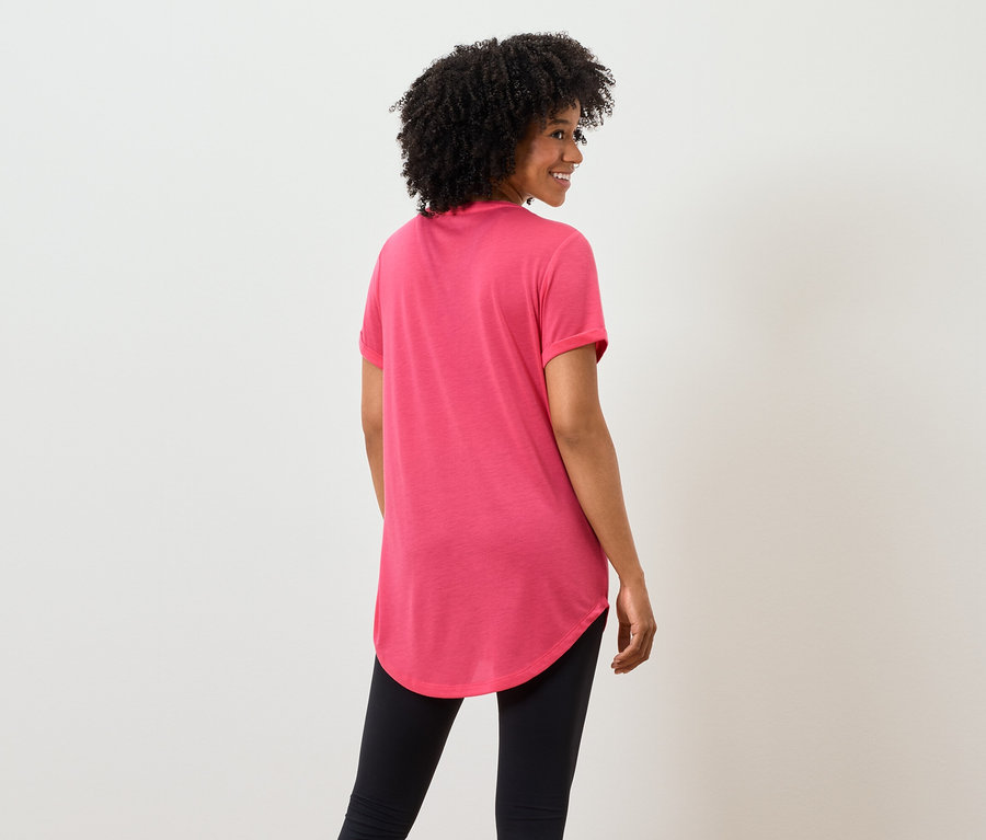 De dos, une femme aux cheveux bouclés portant un t-shirt rose et un legging noir.
