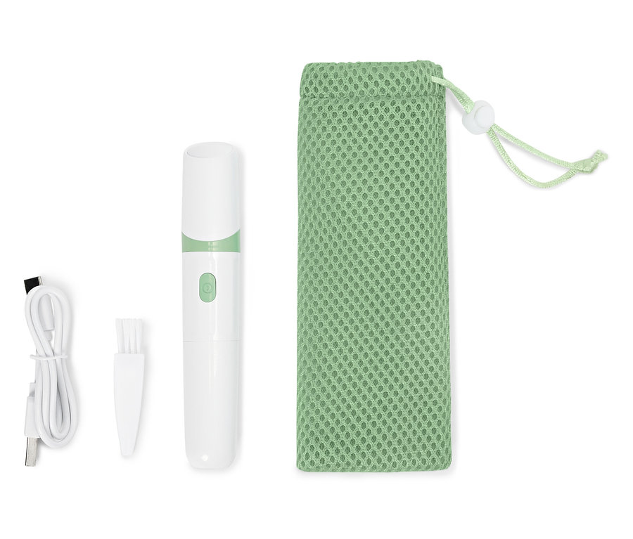 Une coupe-ongles électrique blanche est posée à côté d'un câble USB, d'une brosse de nettoyage et d'un sac en filet vert.