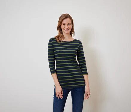 Une femme aux cheveux bruns pose dans un t-shirt rayé bleu-vert et un jean bleu.