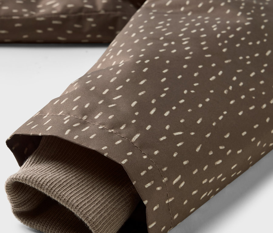 Détail d'une veste de pluie thermique pour enfant, tissu marron avec des points blancs et manche marron.