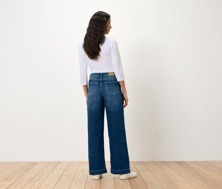 Une femme, dos à la caméra, porte un jean bleu large et une chemise blanche.