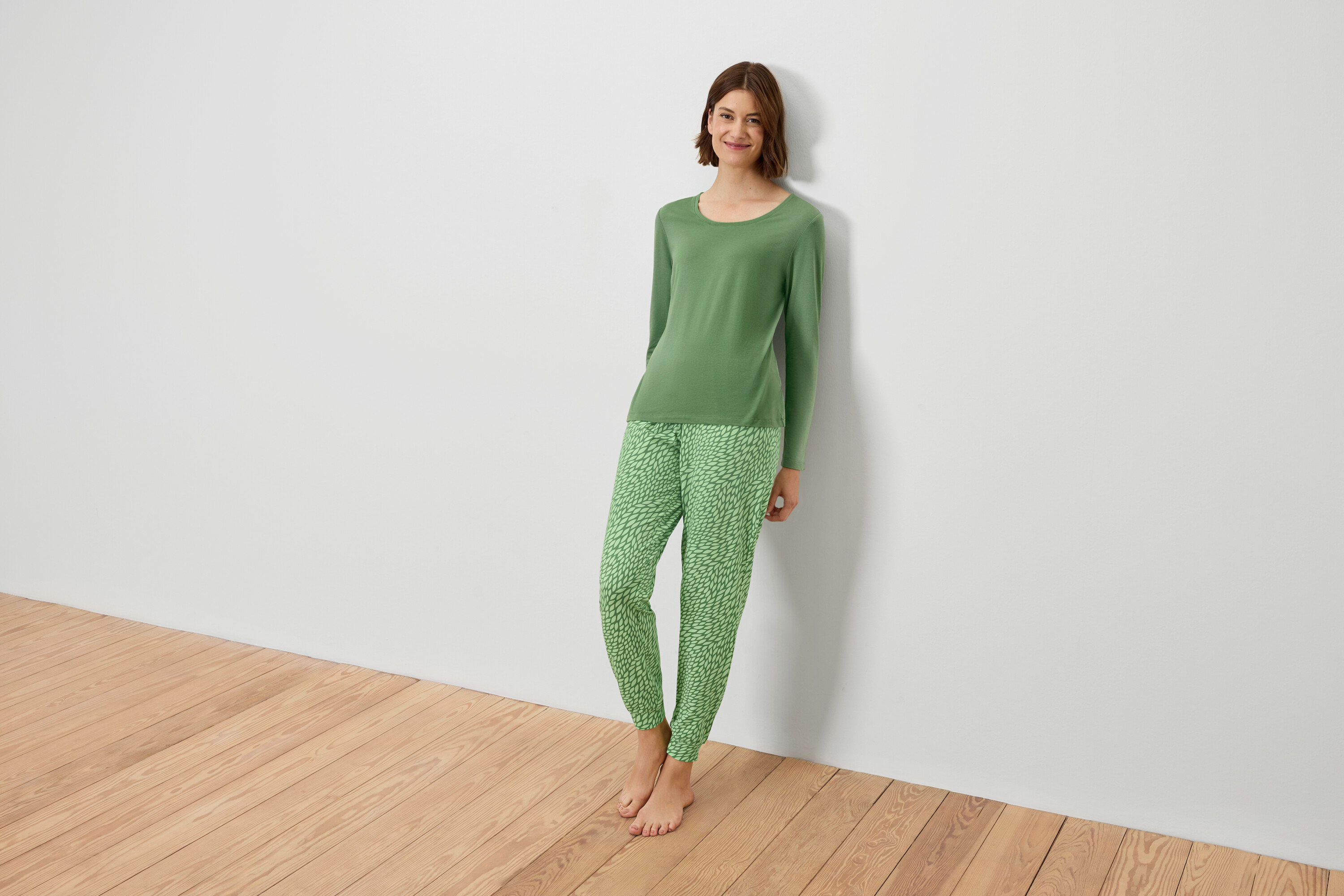 Une femme en pyjama vert est adossée à un mur blanc.