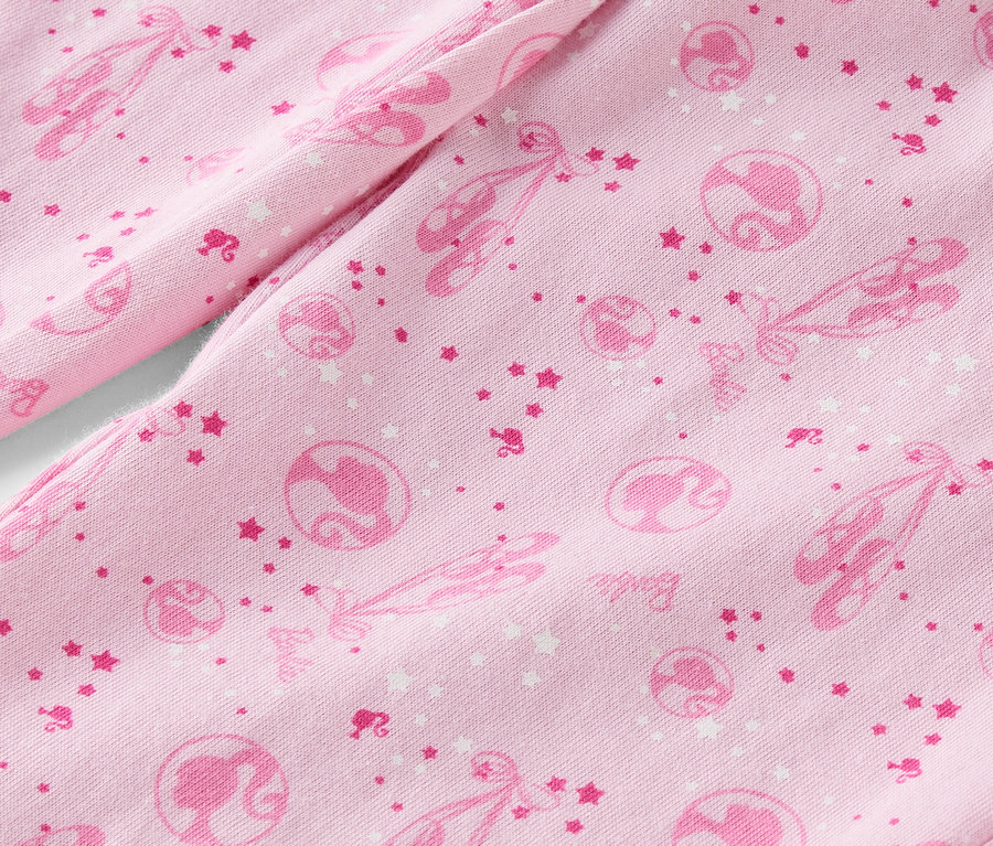 Gros plan sur un tissu rose imprimé avec des chaussons de ballet, des étoiles et des silhouettes de Barbie.