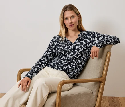 Une femme est assise dans un fauteuil et porte un haut bleu et blanc et un pantalon crème.