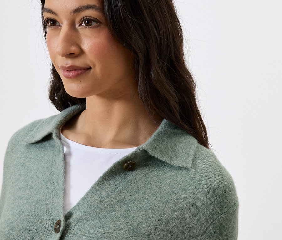 Portrait d'une femme aux cheveux foncés portant un pull vert avec un col et des boutons.