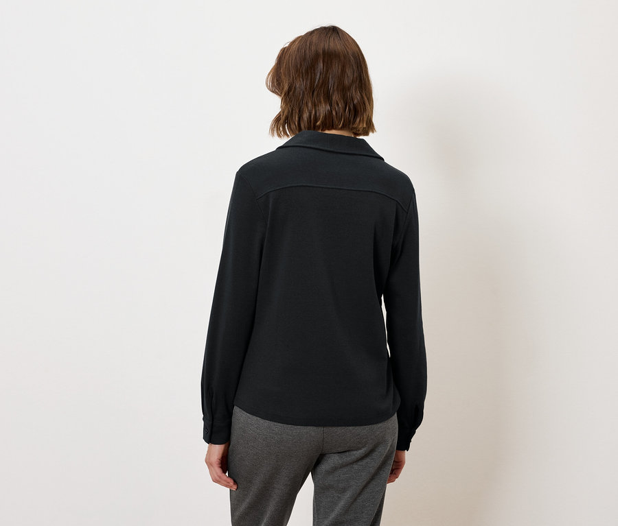 Femme portant une chemise noire à manches longues et un pantalon gris.