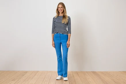 Une femme debout porte un pantalon bleu, un t-shirt rayé et des chaussures blanches.