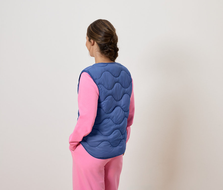 Une femme, dos à la caméra, porte un gilet bleu matelassé sur un pyjama rose.