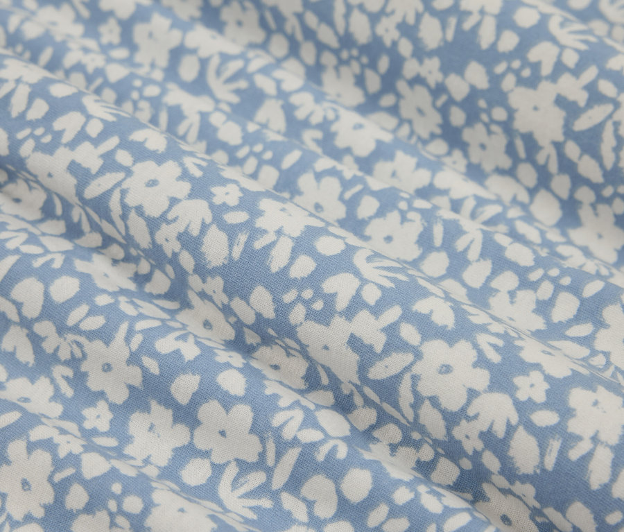 Gros plan d'un tissu bleu avec de petites fleurs blanches, créant un motif délicat et frais.