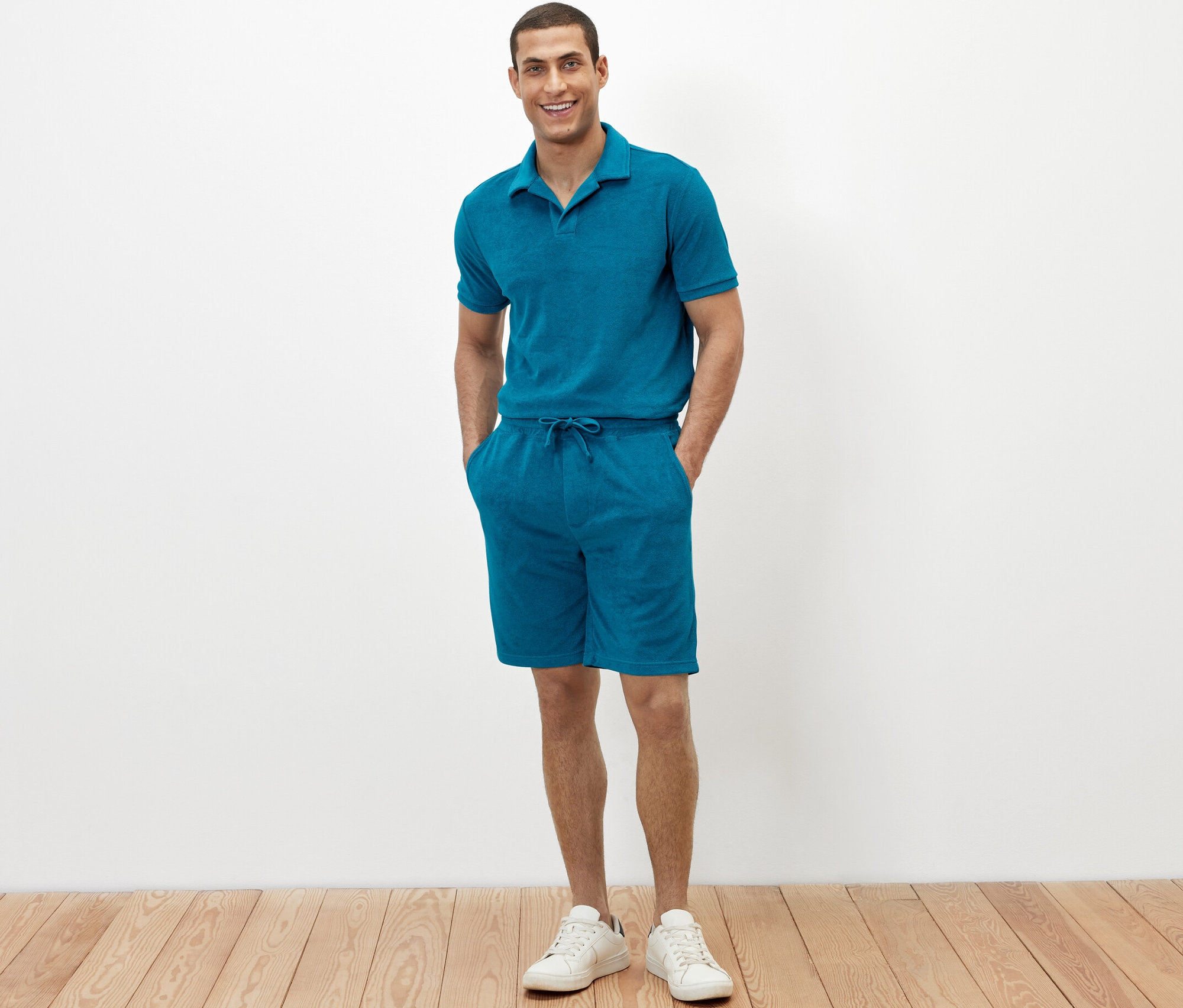 Un homme se tient debout, les mains dans les poches de son short en tissu éponge pétrole.