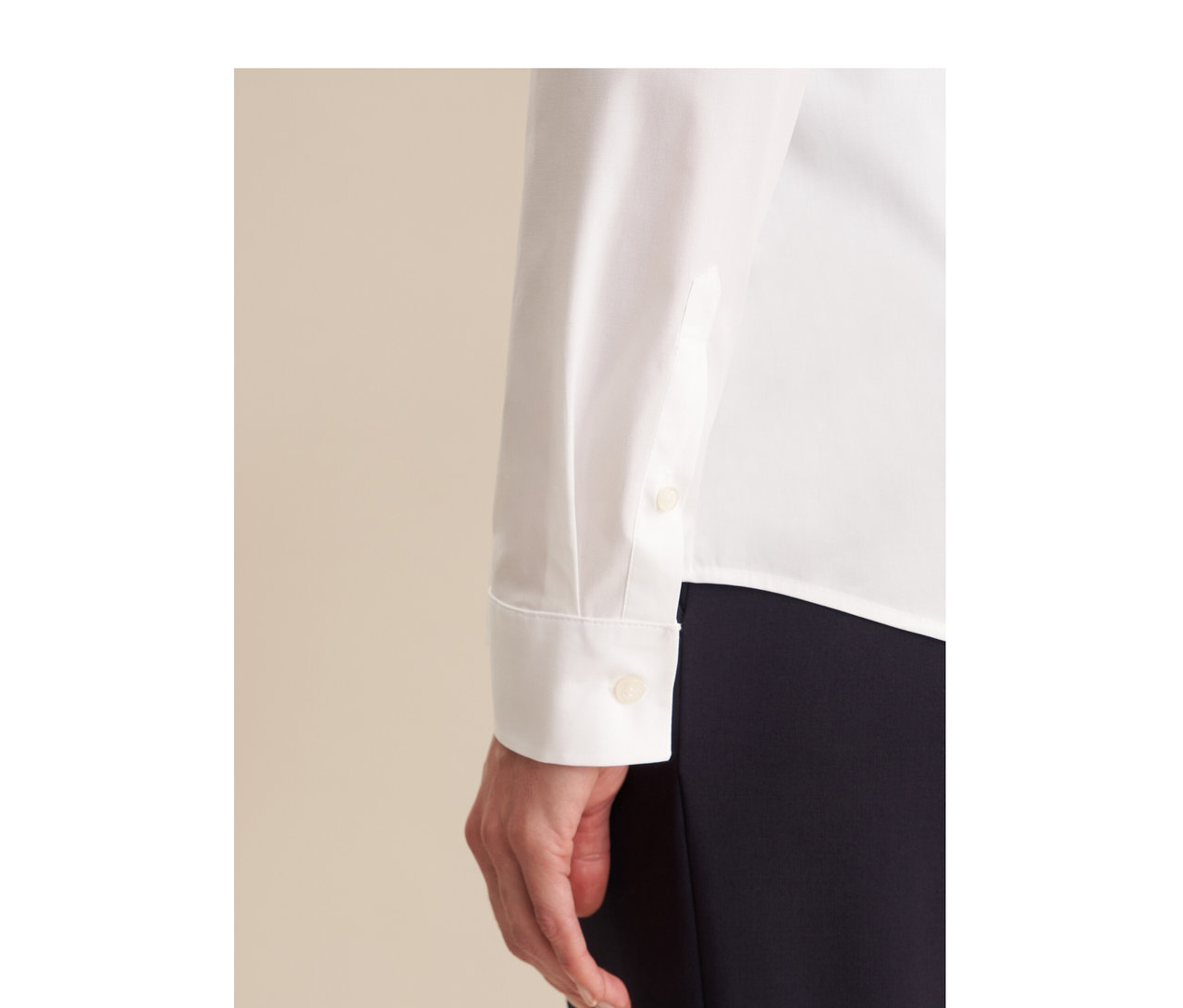 Gros plan d'une personne portant un chemisier Seidensticker Slimfit blanc à manches longues avec poignets boutonnés et un pantalon foncé. Une main est visible.