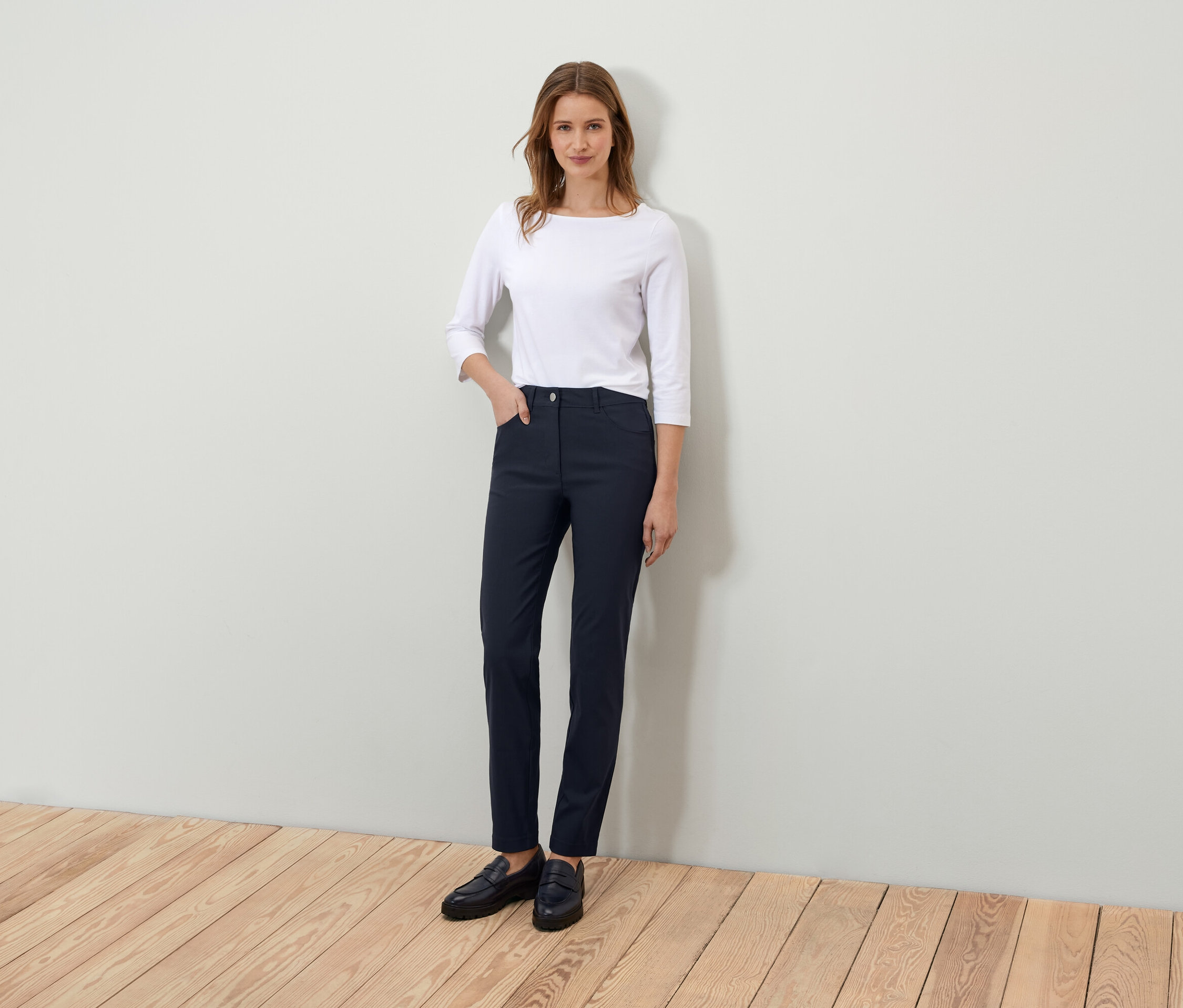 Une femme debout pose dans un t-shirt blanc à manches trois-quarts et un pantalon bleu marine.