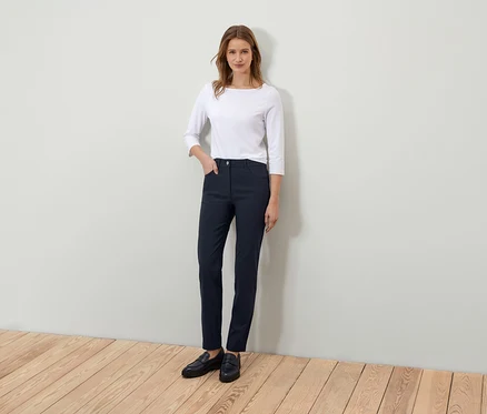 Une femme debout pose dans un t-shirt blanc à manches trois-quarts et un pantalon bleu marine.