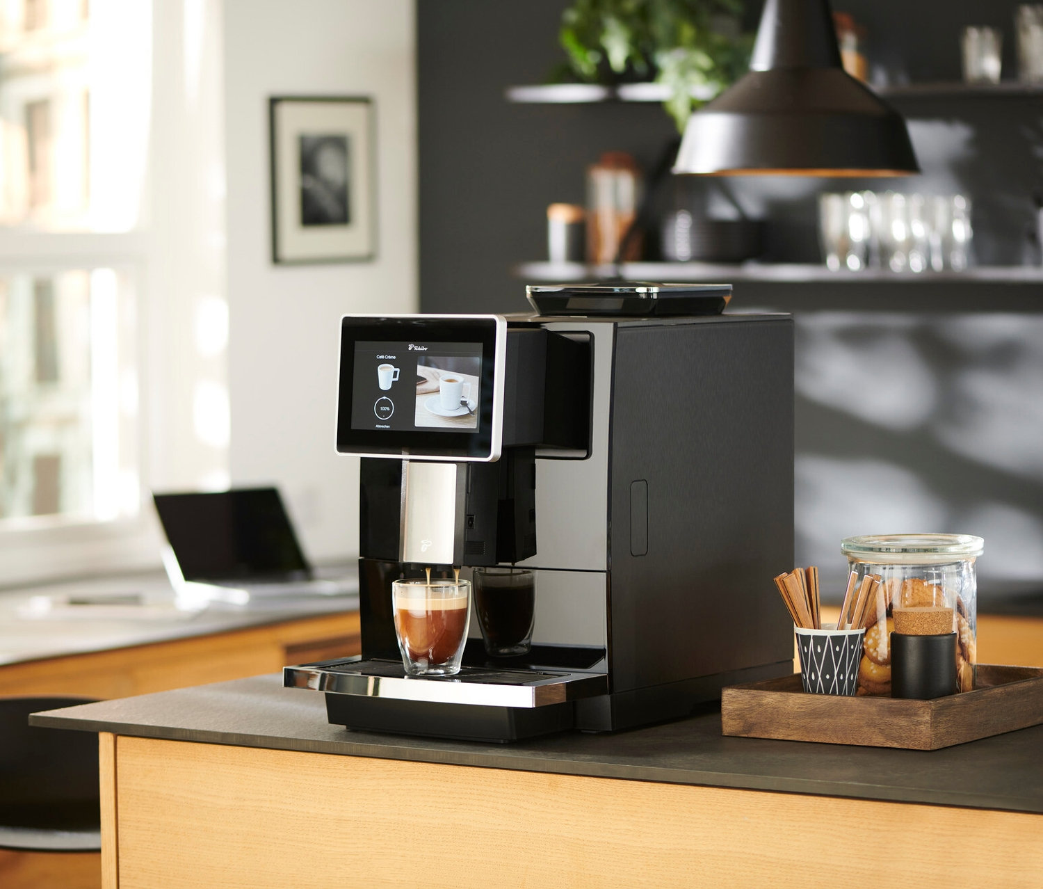 Un préparateur de café automatique remplit un verre de café sur un comptoir de cuisine à côté d'un verre de biscuits.