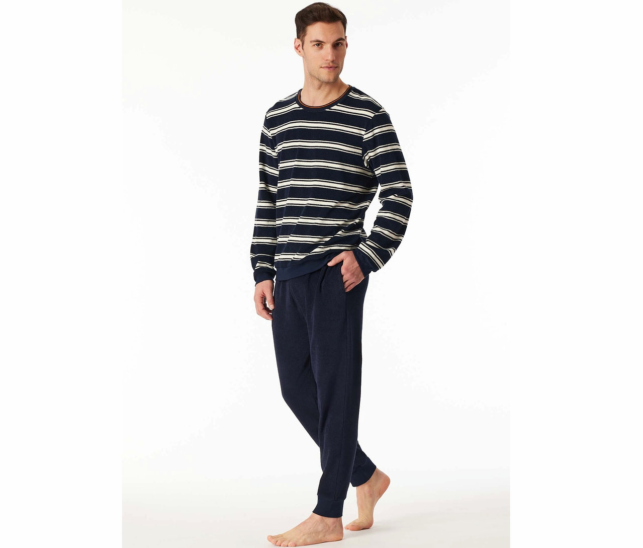 Un homme debout, portant un haut rayé et un pantalon bleu marine.