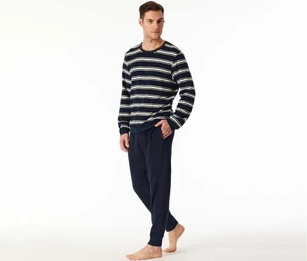 Homme portant un ensemble pyjama en tissu éponge SCHIESSER, avec un haut rayé bleu marine et blanc à manches longues et un pantalon bleu marine, debout pieds nus, une main dans la poche.