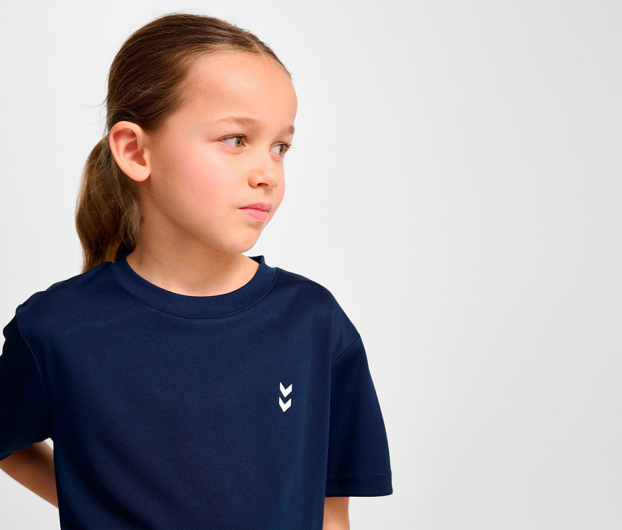 Portrait d'une jeune fille aux cheveux bruns portant un t-shirt d'entraînement bleu foncé HUMMEL HMLJR pulse.