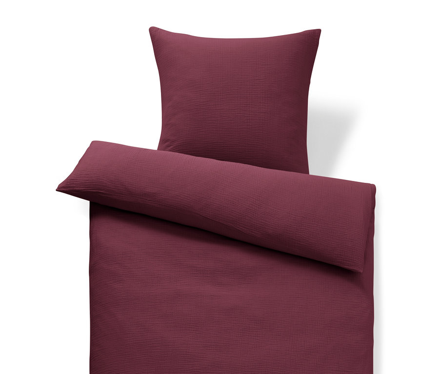 Linge de lit bordeaux et oreiller sur fond blanc.