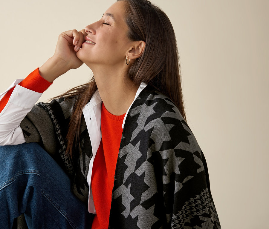 Une femme est assise et porte un pull orange en maille fine de laine mérinos.
