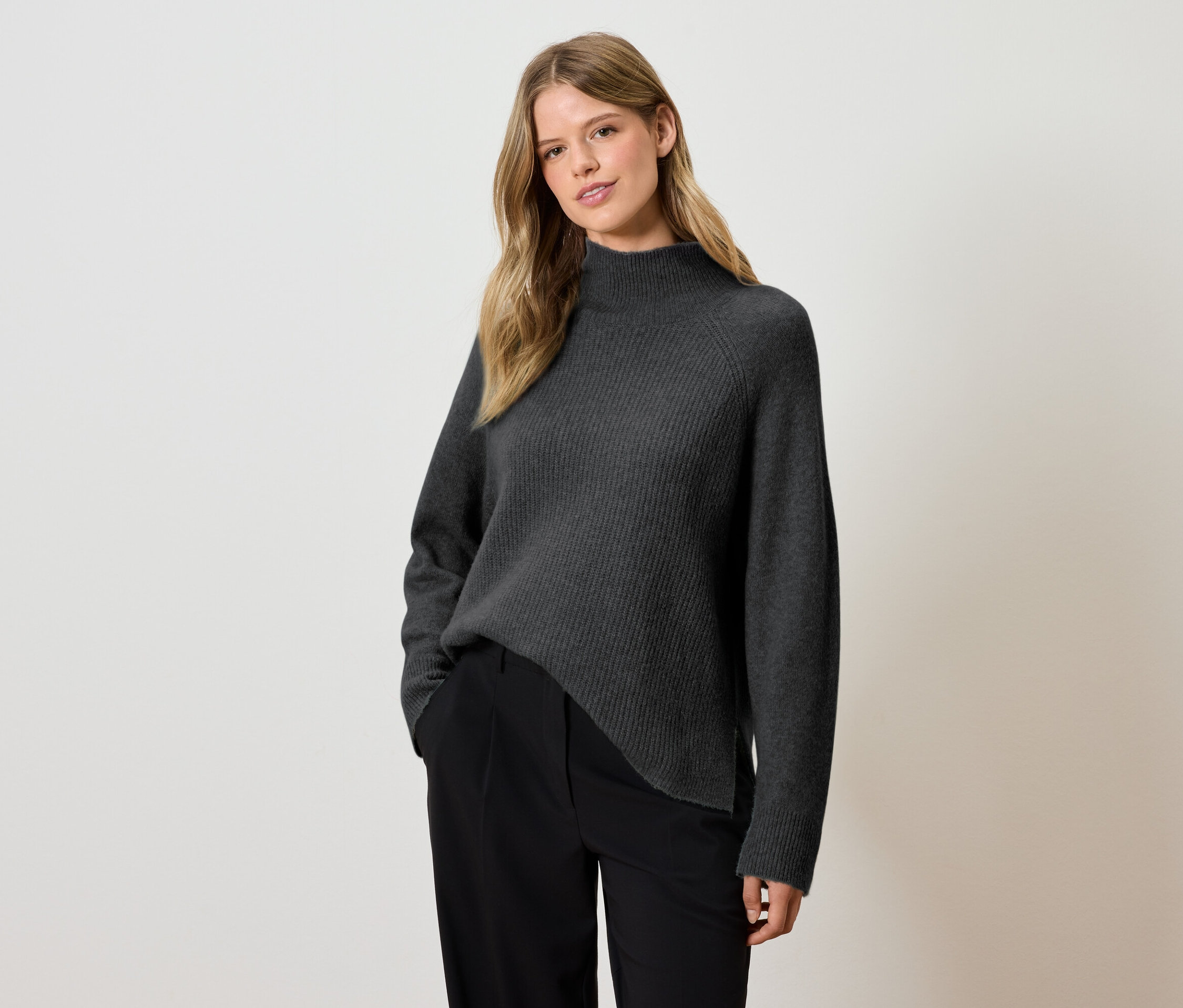 Une femme pose en pull gris et pantalon noir.