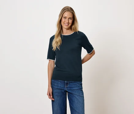 Une femme aux cheveux blonds porte un haut à manches courtes bleu foncé et un jean.