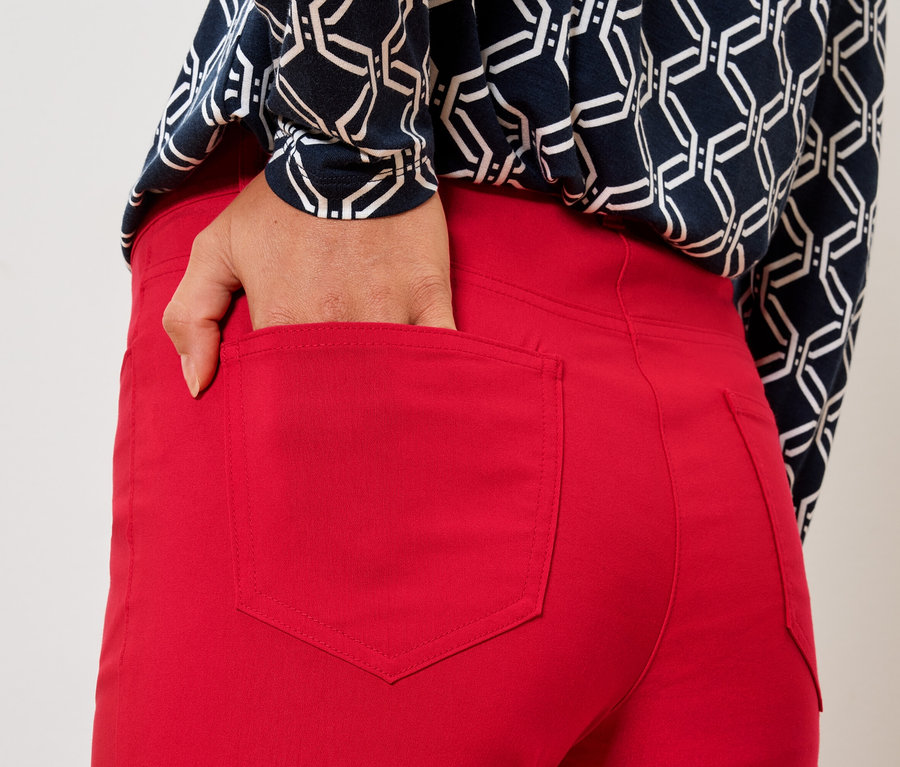 Une femme met sa main dans la poche arrière d'un pantalon rouge.