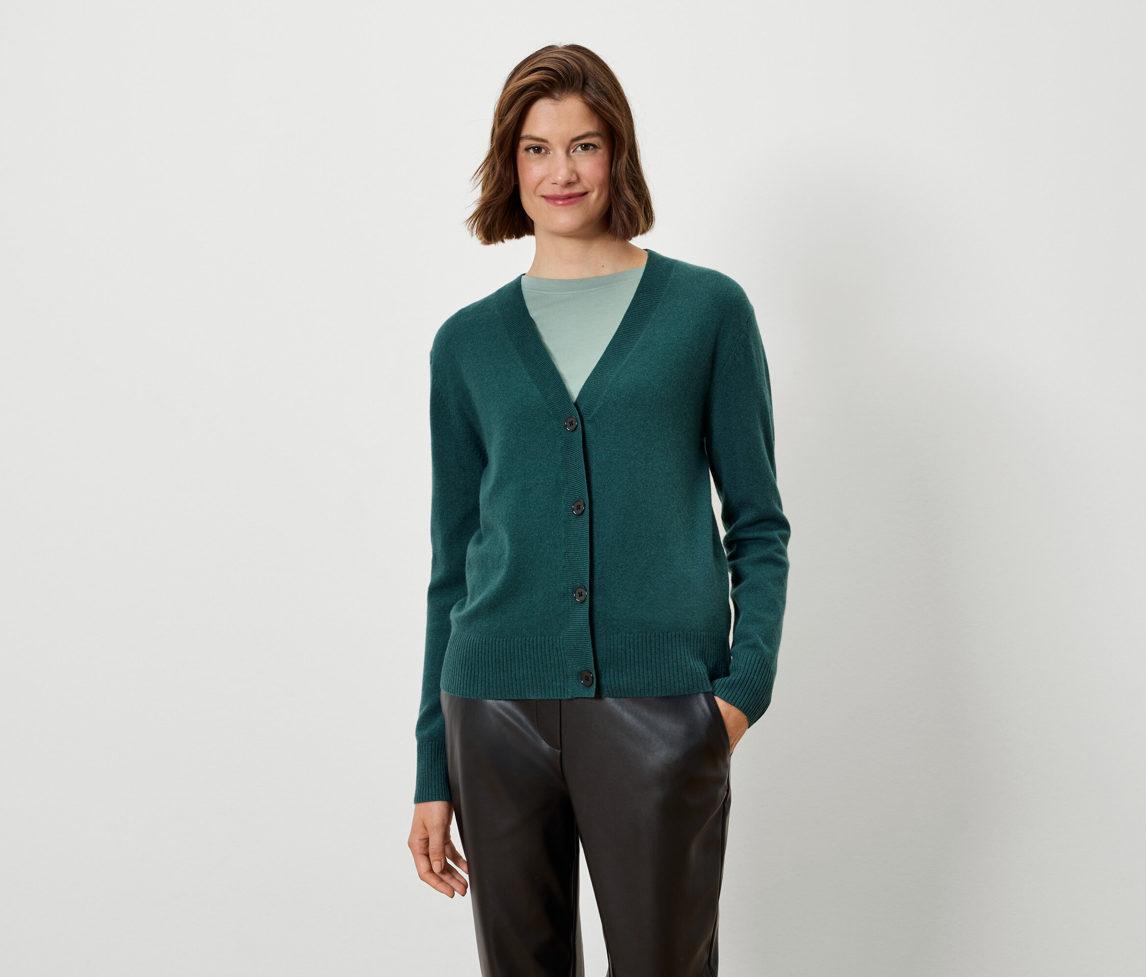 Une femme porte un cardigan vert et un pantalon noir.