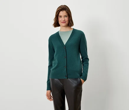 Une femme porte un cardigan vert et un pantalon noir.
