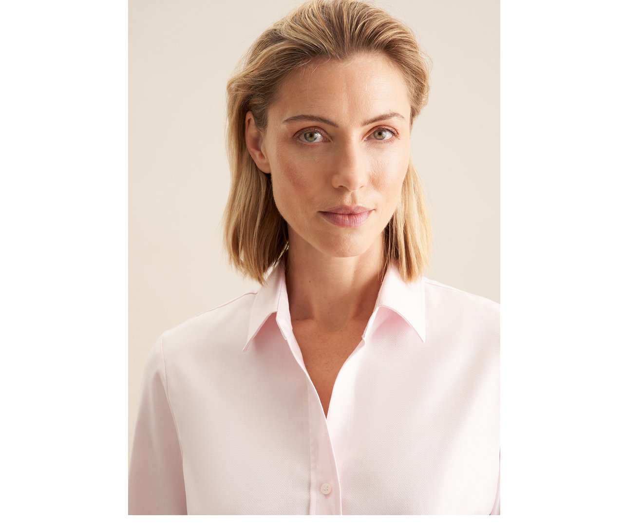 Femme blonde portant un chemisier en tulle Seidensticker rose, regardant la caméra.